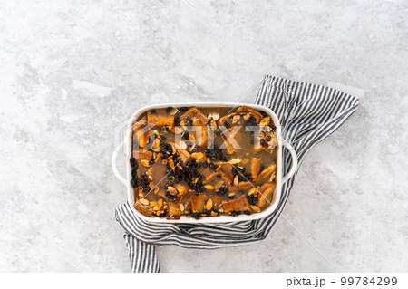 Flat lay. Cooling freshly baked bread pudding with raising and almond slivers in a white casserole dish. 99784299