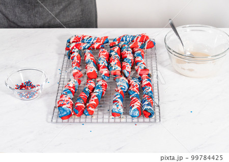 Drizzling white glaze on top of patriotic cinnamon twists. and decorating with star sprinkles. 99784425
