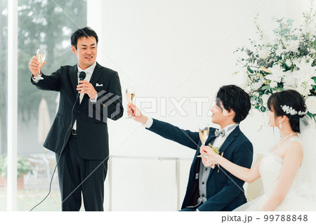 結婚式で乾杯の挨拶をする男性と新郎新婦 99788848