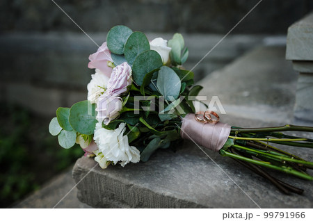 A pair of gold wedding rings on a bride's bouquet with colorful flowers 99791966