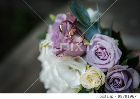 A pair of gold wedding rings on a bride's bouquet with colorful flowers 99791967