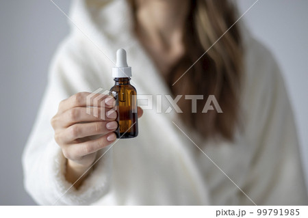 The Young Woman's hand holds a bottle with a dropper, with an oil or serum for facial and body care. Selective Focus. The Young Woman's hand holds a bottle with a dropper, with an oil or serum for facial and body care. Selective Focus. 99791985