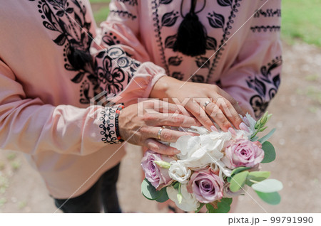 Hands of the newlyweds with wedding rings on the wedding bouquet. Hands of the bride and groom on a bouquet of flowers Hands of the newlyweds with wedding rings on the wedding bouquet. Hands of the bride and groom on a bouquet of flowers 99791990
