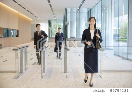 セキュリティゲートを通ってオフィスビルに入る男女のビジネスパーソン 99794181