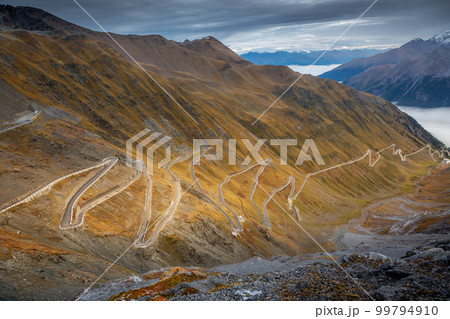 Stelvio pass, mountain road dramatic landscape at dawn above mist, Italy 99794910