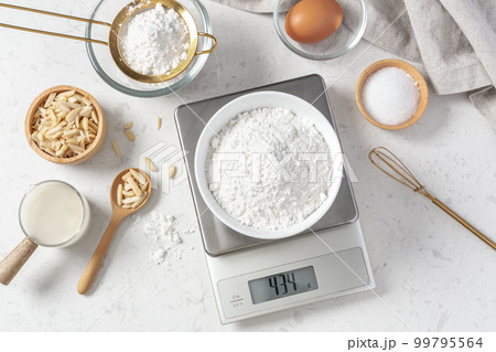 Flour in white bowl measuring on digital scale with cake or bakery ingredients and utensil on marble kitchen table, top view 99795564