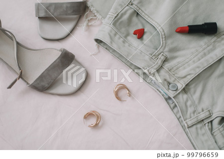 Overhead view of woman's casual spring outfit with jeans, sandals, red lipstick and earrings on beige background, Flat lay, top view Overhead view of woman's casual spring outfit with jeans, sandals, red lipstick and earrings on beige background, Flat lay, top view 99796659