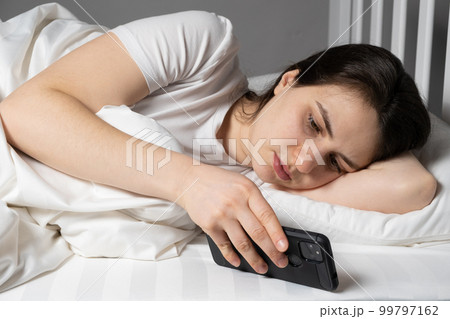 A woman lies in bed and reads the news or watches something on a smartphone before going to bed, gadgets in bed A woman lies in bed and reads the news or watches something on a smartphone before going to bed, gadgets in bed 99797162