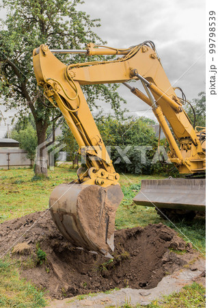 A bucket of excavator pours the ground into a heap against the background of a rural industrial zone. Bulldozer work on the construction site A bucket of excavator pours the ground into a heap against the background of a rural industrial zone. Bulldozer work on the construction site 99798539