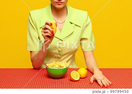 Cropped image of woman in retro suit squeezing lemon juice into cereal against pink studio background. Food pop art photography. 99799450
