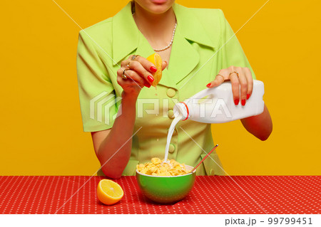 Cropped image of woman in retro suit putting milk and squeezing lemon juice into cereal against pink studio background. Food pop art photography. 99799451