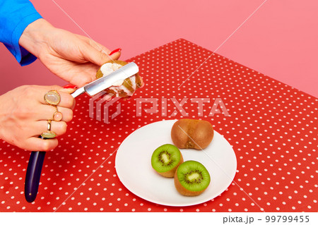 Female hand putting sause on kiwi with razor against pink studio background. Food pop art photography. Creativity and art Female hand putting sause on kiwi with razor against pink studio background. Food pop art photography. Creativity and art 99799455