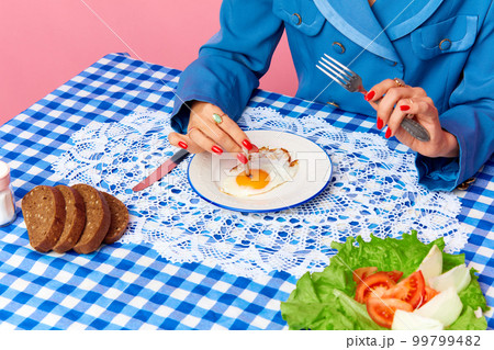 Top view image of female hand putting cigarette into egg yolk on fried eggs at checkered retro tablecloth. Food pop art photography. 99799482