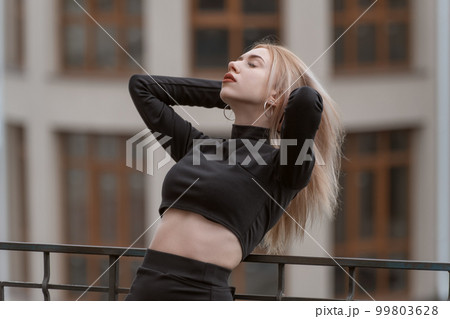 Portrait of young attractive woman in black short top threw her head back and adjusts her hair. Girl in the city Portrait of young attractive woman in black short top threw her head back and adjusts her hair. Girl in the city 99803628
