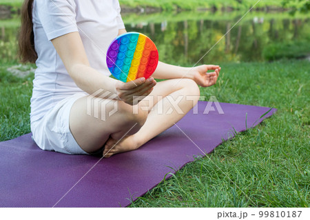 A woman meditates in nature and eats a reusable bubble wrap pop it antistress toy. Deal with stress at work with Pop it, yoga and meditation. 99810187