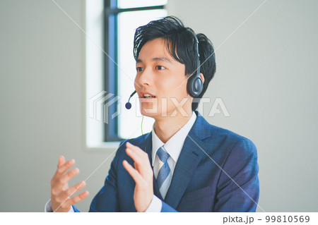 ヘッドセットをつけてインサイドセールスをするスーツ姿の若い男性 99810569