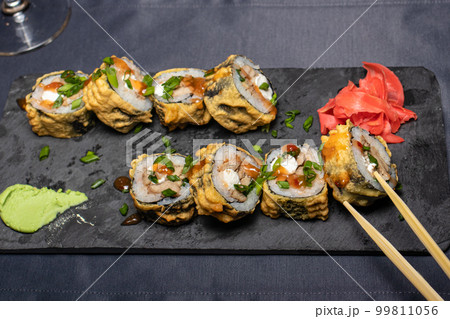 A man holds a roll with wooden sticks for sushi. Sea food, raw fish, Japanese traditional cuisine. A man holds a roll with wooden sticks for sushi. Sea food, raw fish, Japanese traditional cuisine. 99811056