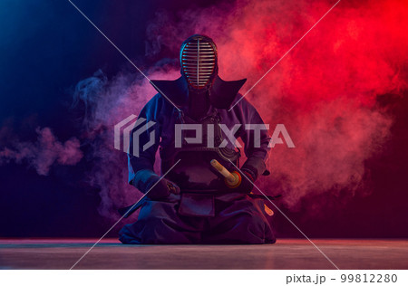 Man, professional kendo athlete, combat sportsman posing with shinai sword against gradient dark background in neon light with smoke 99812280