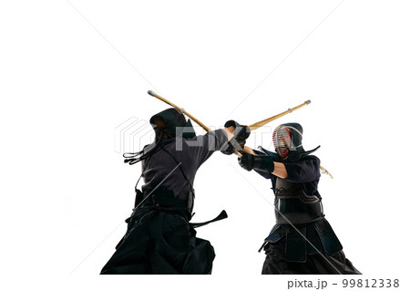 Dynamic image of two men, professional kendo athletes in special uniform training, fighting with shinai sword against white studio background 99812338