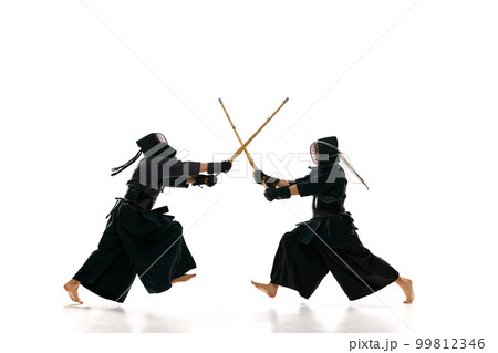 Dynamic image of two men, professional kendo athletes training with bamboo shinai sword against white studio background Dynamic image of two men, professional kendo athletes training with bamboo shinai sword against white studio background 99812346