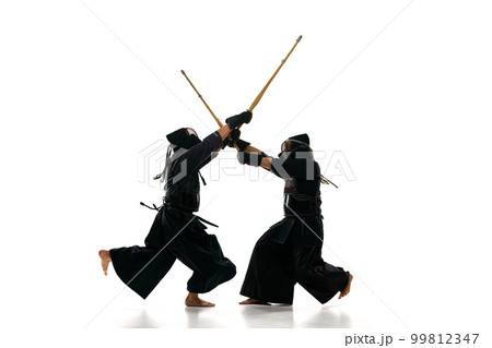 Dynamic image of two men, professional kendo athletes in uniform with helmet training with bamboo shinai sword against white studio background Dynamic image of two men, professional kendo athletes in uniform with helmet training with bamboo shinai sword against white studio background 99812347