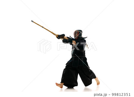 Man, professional kendo athlete in motion, in uniform training with bamboo sword, shinai against white studio background 99812351