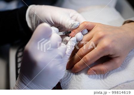 The beautician applies a base coat to the client's nails. The beautician applies a base coat to the client's nails. 99814619