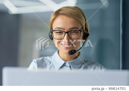 Young female office worker close up, businesswoman with headset phone for video call talking to client remotely, customer support tech worker talking and consulting, successful woman at work. 99814701