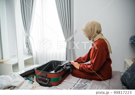 Asian woman in veil puts clothes in a suitcase Asian woman in veil puts clothes in a suitcase 99817223
