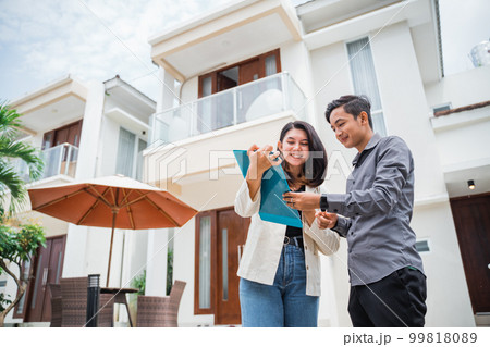 Asian female real estate agent showing clipboard chatting with man 99818089