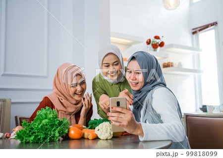 friend with hijab looking at the phone to make food 99818099