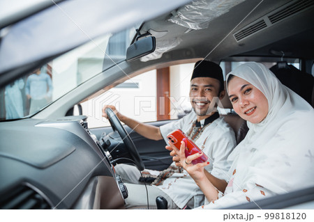Asian Muslim husband and wife using cell phone in car 99818120