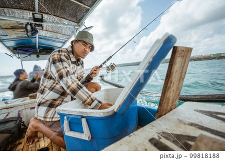 Asian fisherman checking bait in box in small fishing boat 99818188