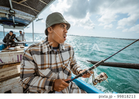 Asian fisherman excited while fishing on small boat at sea 99818213