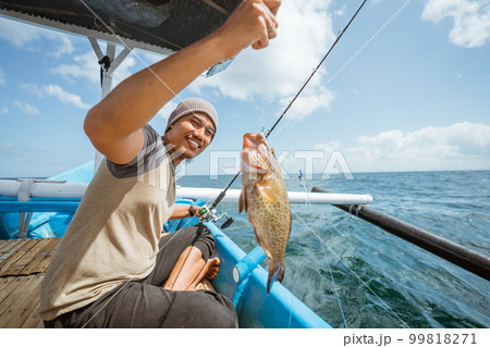 Asian fisherman catches grouper in the sea while fishing 99818271