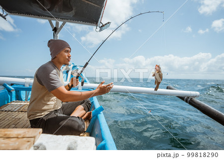 Asian angler pulls the rod when he catches a fish 99818290