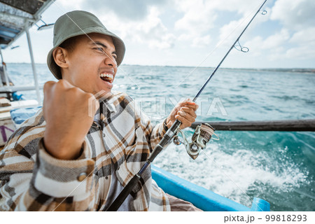 excited Asian fisherman on Strike when fishing at sea 99818293