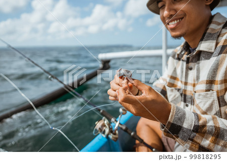 Asian angler puts bait on a hook while casting 99818295