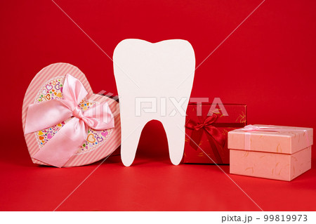 Valentine's Day in dentistry - a large white tooth, a heart and boxes of gifts on a red background, a place for text Valentine's Day in dentistry - a large white tooth, a heart and boxes of gifts on a red background, a place for text 99819973