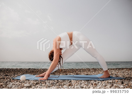 Woman sea yoga. Well looking middle aged woman with braids dreadlocks in white leggings and tops doing stretching pilates on yoga mat near sea. Female fitness yoga routine concept. Healthy lifestyle. 99835750