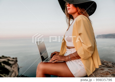 Digital nomad, Business woman working on laptop by the sea. Pretty lady typing on computer by the sea at sunset, makes a business transaction online from a distance. Freelance, remote work on vacation Digital nomad, Business woman working on laptop by the sea. Pretty lady typing on computer by the sea at sunset, makes a business transaction online from a distance. Freelance, remote work on vacation 99835796