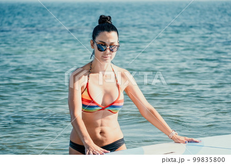 Sea woman sup. Silhouette of happy middle aged tanned woman in rainbow bikini, surfing on SUP board, confident paddling through water surface. Idyllic sunset. Active lifestyle at sea or river. 99835800