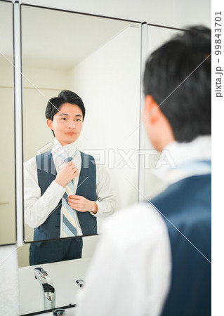 鏡の前でネクタイを締める若いサラリーマンの男性 99843701