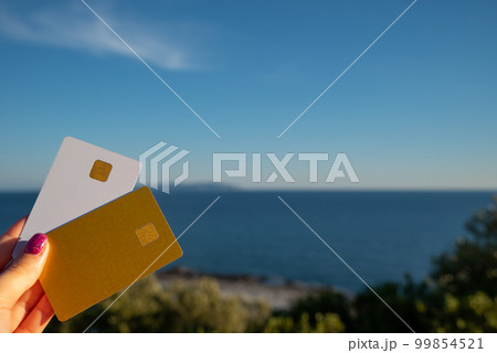 Golden and White Bank Card In Woman Hand On Background Of Scenic View From Arkoudilas Viewpoint, Mountains, Ionian Sea Corfu, Greece. The Concept Of Payment For Relax, Unlimited Possibilities. 99854521