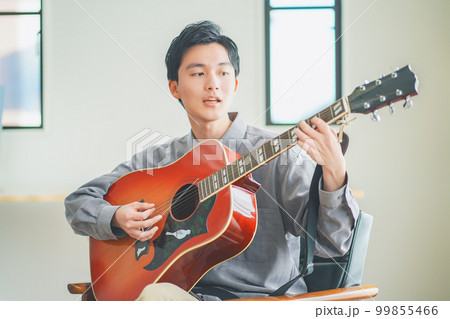自宅でアコースティックギターを弾く若い男性 99855466