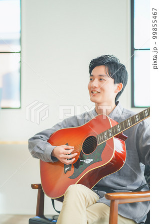 自宅でアコースティックギターを弾く若い男性 99855467
