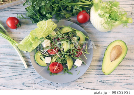 Salad of microgreens, avocado, tomatoes, cheese and arugula, on a plate, against the background of fennel and greens, recipe from natural ingredients, healthy food  99855955