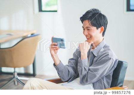 ソファに座ってスマートフォンで動画を見る若い男性 99857276