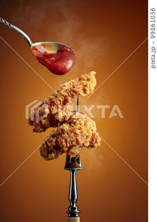 Fried chicken with ketchup on a fork. 99861036