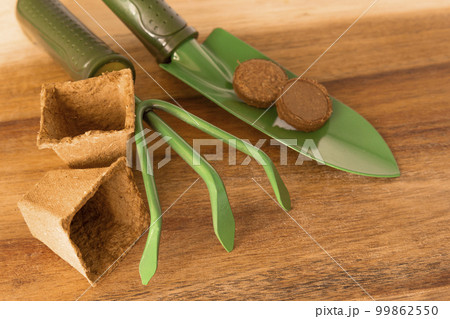 Biodegradable pot, peat tablets, garden tools trowel, rake on wooden background. Gardening concept. Biodegradable pot, peat tablets, garden tools trowel, rake on wooden background. Gardening concept. 99862550